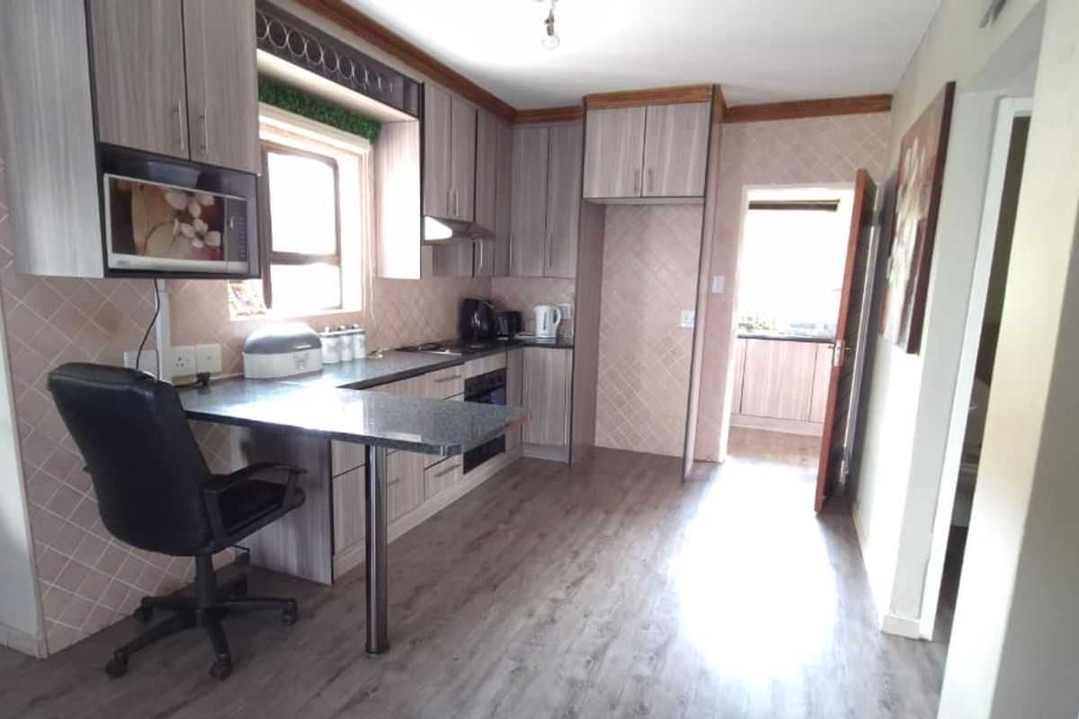 A functional kitchen featuring wood-look cabinetry, integrated oven, and a breakfast bar, with a connecting doorway leading to a secondary utility or scullery area.