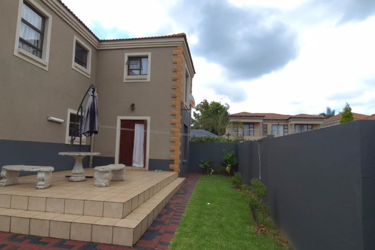 A rear view of the property featuring a raised tiled patio area, a small lawn, and a perimeter boundary wall.