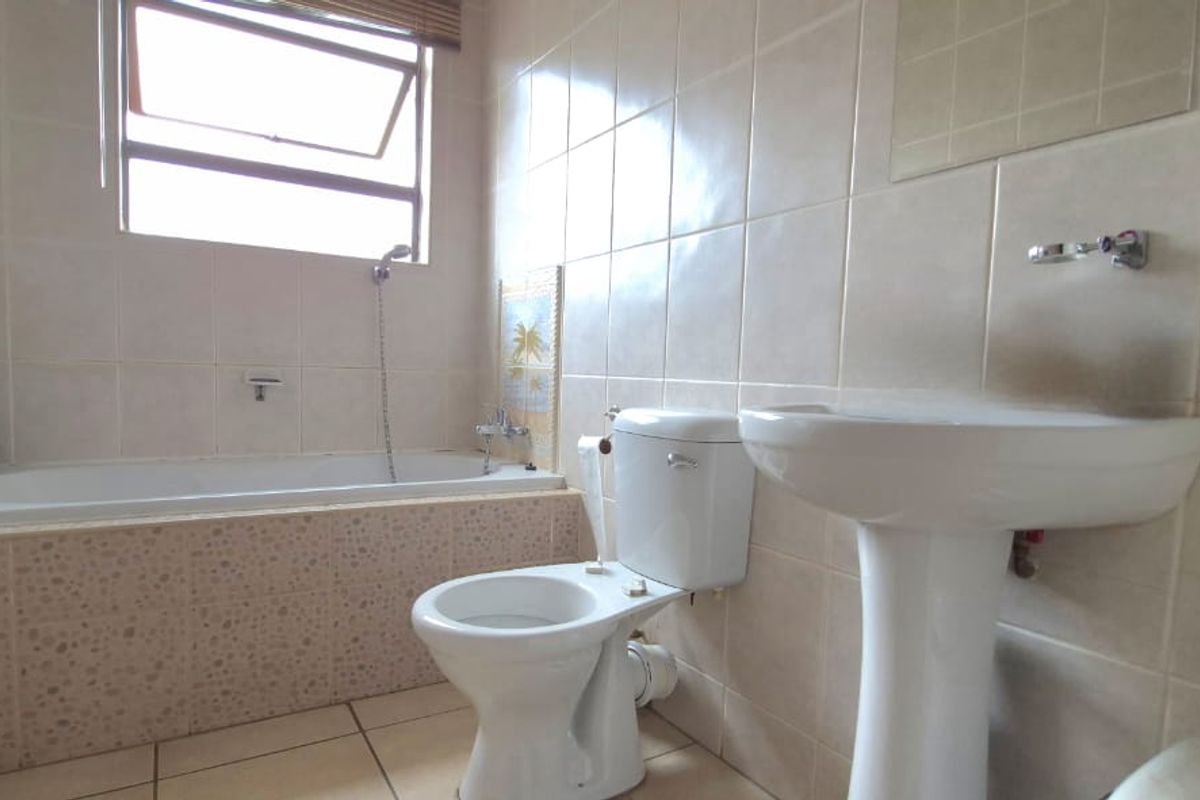 A functional bathroom featuring a built-in bathtub, pedestal sink, and toilet with neutral wall tiling and natural light from a window.