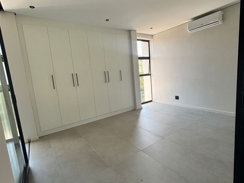 A bright, modern bedroom featuring large-format floor tiles, extensive built-in cabinetry, and a wall-mounted air conditioning unit.