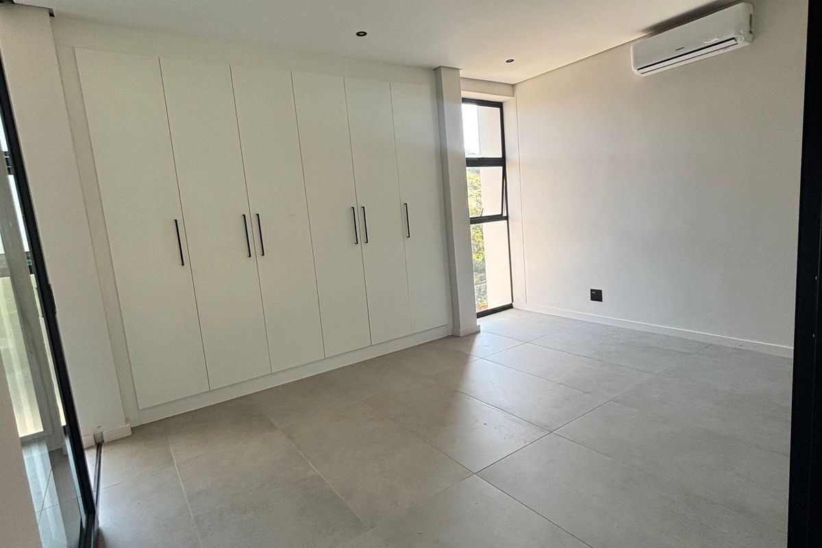A bright, modern bedroom featuring large-format floor tiles, extensive built-in cabinetry, and a wall-mounted air conditioning unit.