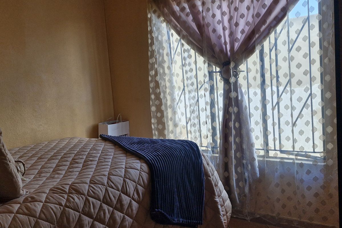 A bedroom featuring a window with fixed security bars and neutral wall finishes.