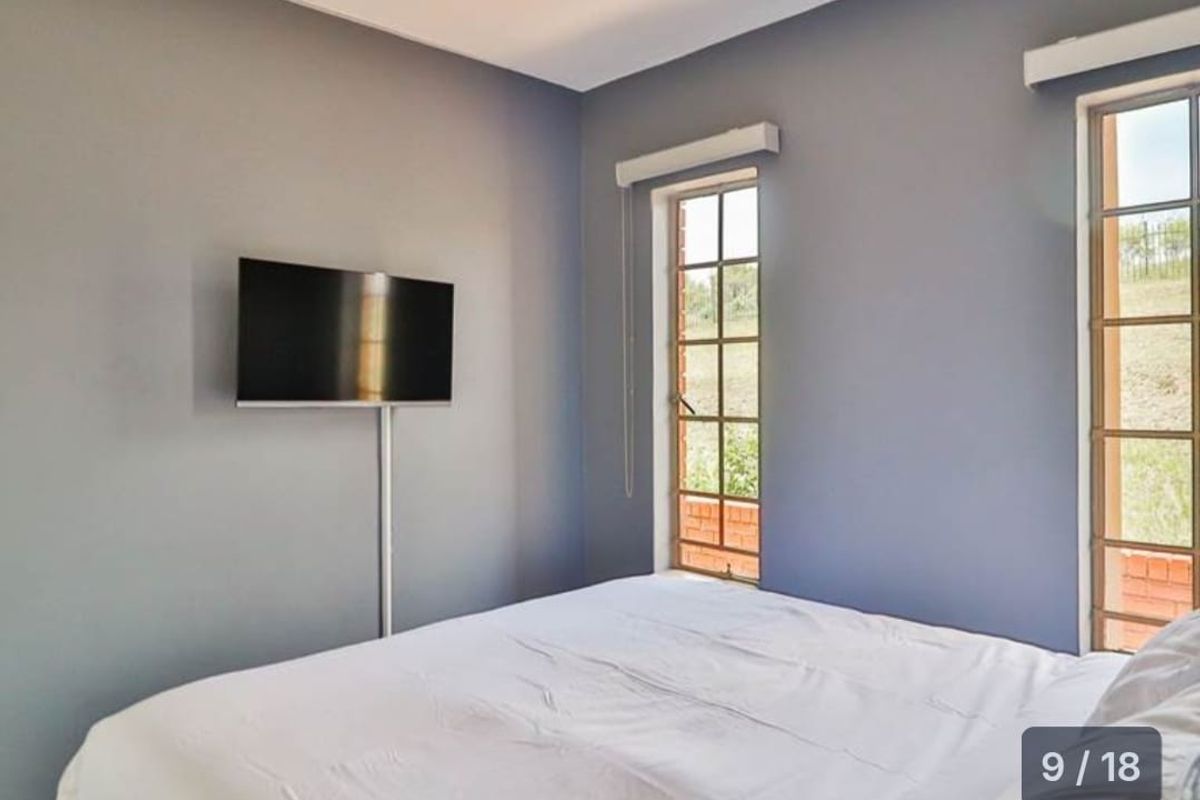 A bedroom featuring grey walls, two windows with metal frames, and a wall-mounted television.