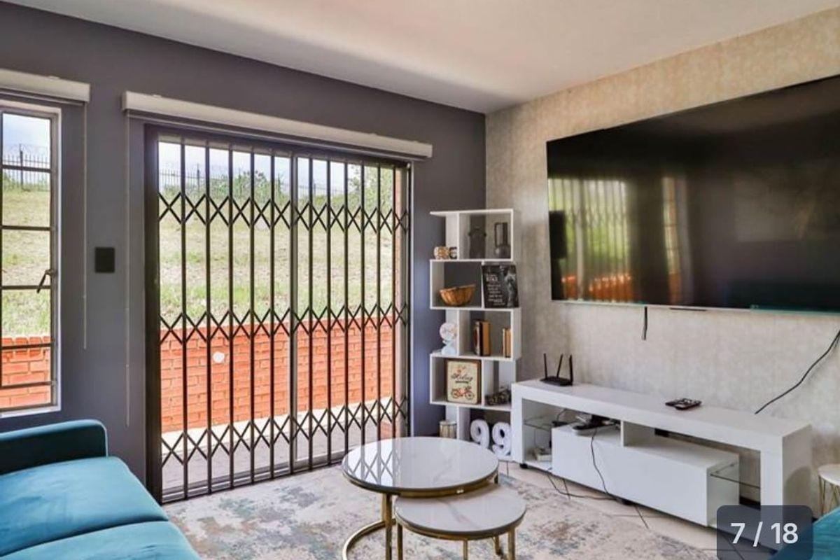 A well-maintained living room featuring a sliding glass door with security gate, tiled flooring, and a feature wall.