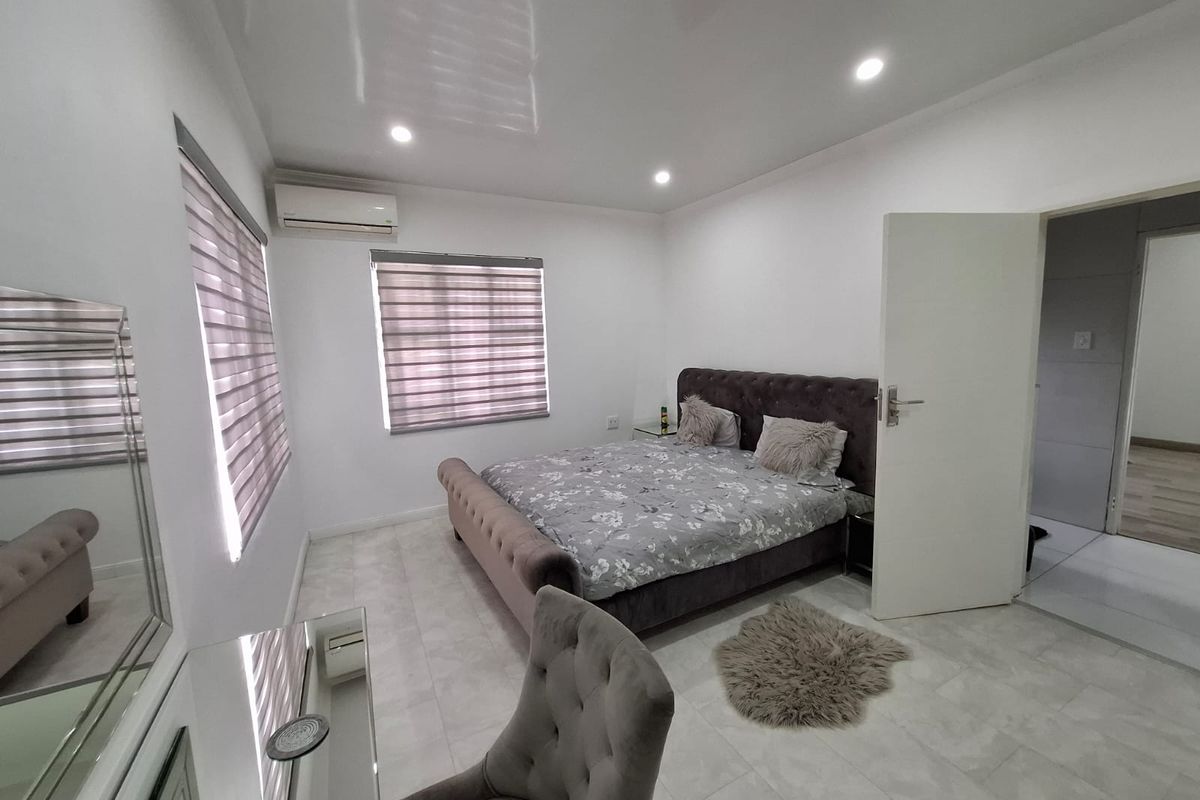 A well-maintained bedroom featuring tiled flooring, recessed ceiling lighting, and a wall-mounted air conditioning unit.