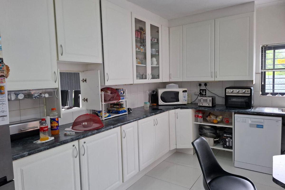 A functional kitchen featuring white cabinetry, dark laminate countertops, tiled flooring, and integrated appliance spaces, offering a clean and practical layout.