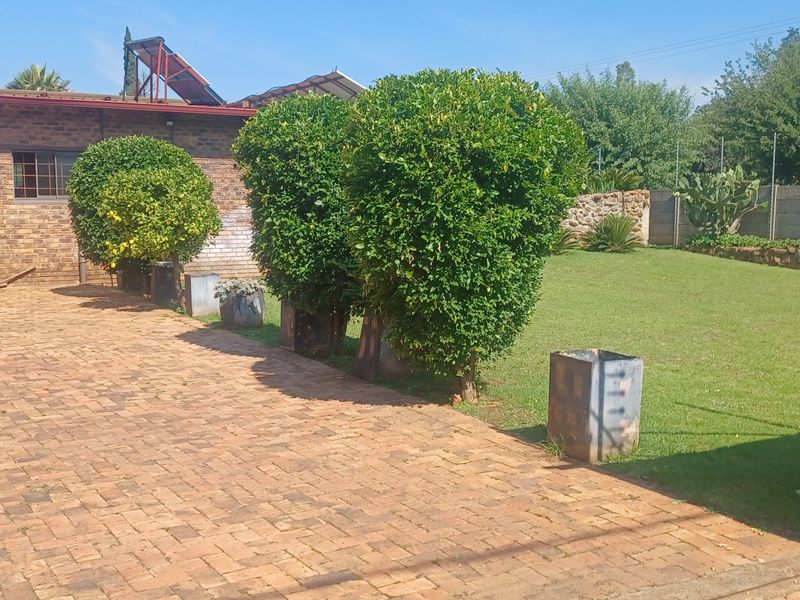 Front exterior view featuring a brick-paved driveway, facebrick house facade, solar water heating system, and a well-maintained lawn with boundary walling.