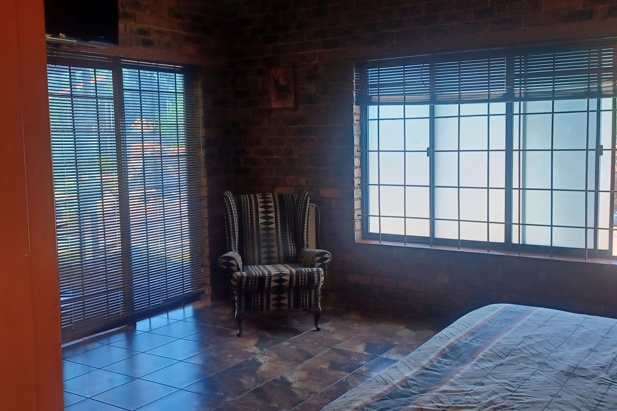 Bedroom featuring exposed brick walls, tiled flooring, and large sliding glass doors with security bars, providing natural light and access to the exterior.