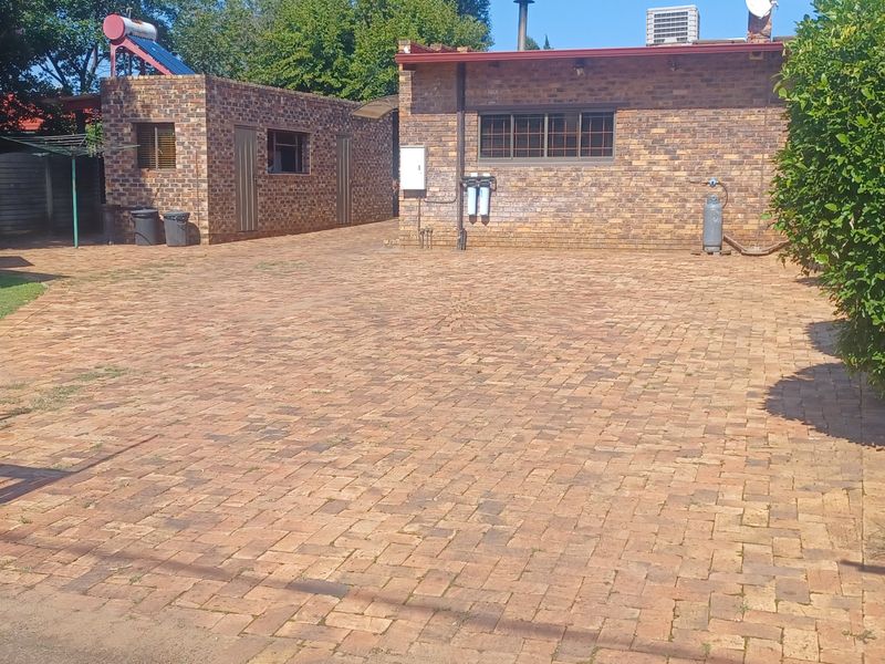 A spacious paved driveway leading to a face brick residential building featuring a solar water heater and external water filtration system.