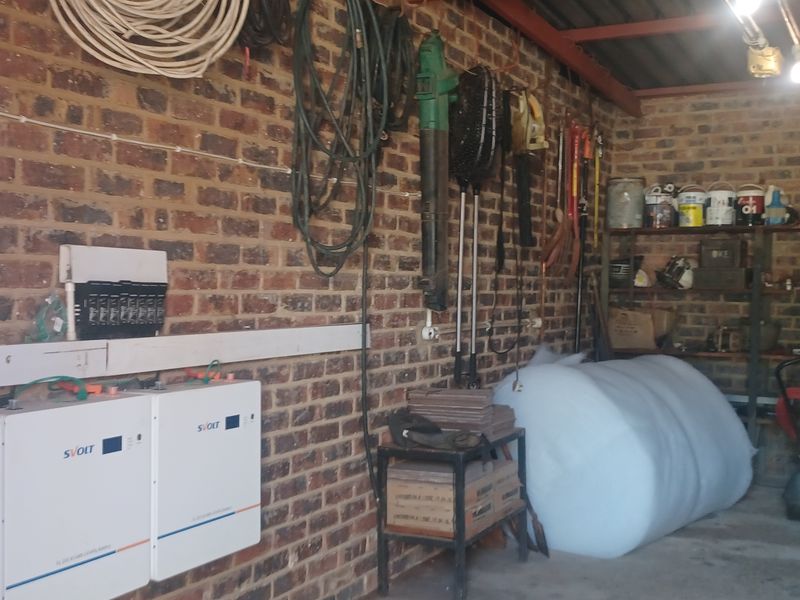 A functional garage space featuring exposed brick walls, integrated solar battery storage units, and built-in metal shelving for storage.