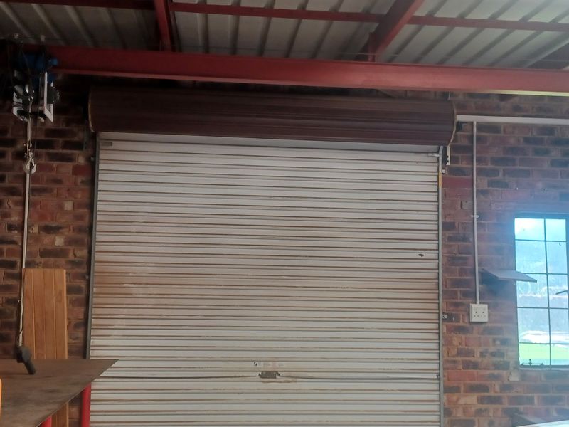 A functional garage space featuring exposed brick walls, steel roof beams, and a secure roller shutter door.