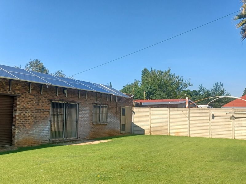 Rear exterior view of a brick building featuring a solar panel installation, roller shutter door, and a spacious lawn enclosed by a precast wall.