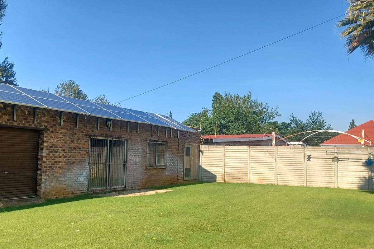 Rear exterior view of a brick building featuring a solar panel installation, roller shutter door, and a spacious lawn enclosed by a precast wall.