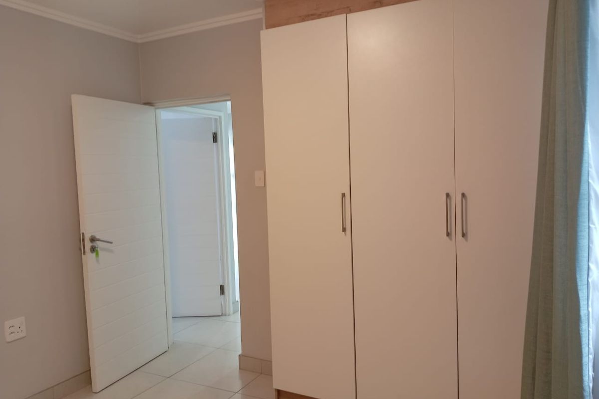 A clean bedroom interior featuring built-in floor-to-ceiling wardrobes with a modern finish and tiled flooring.