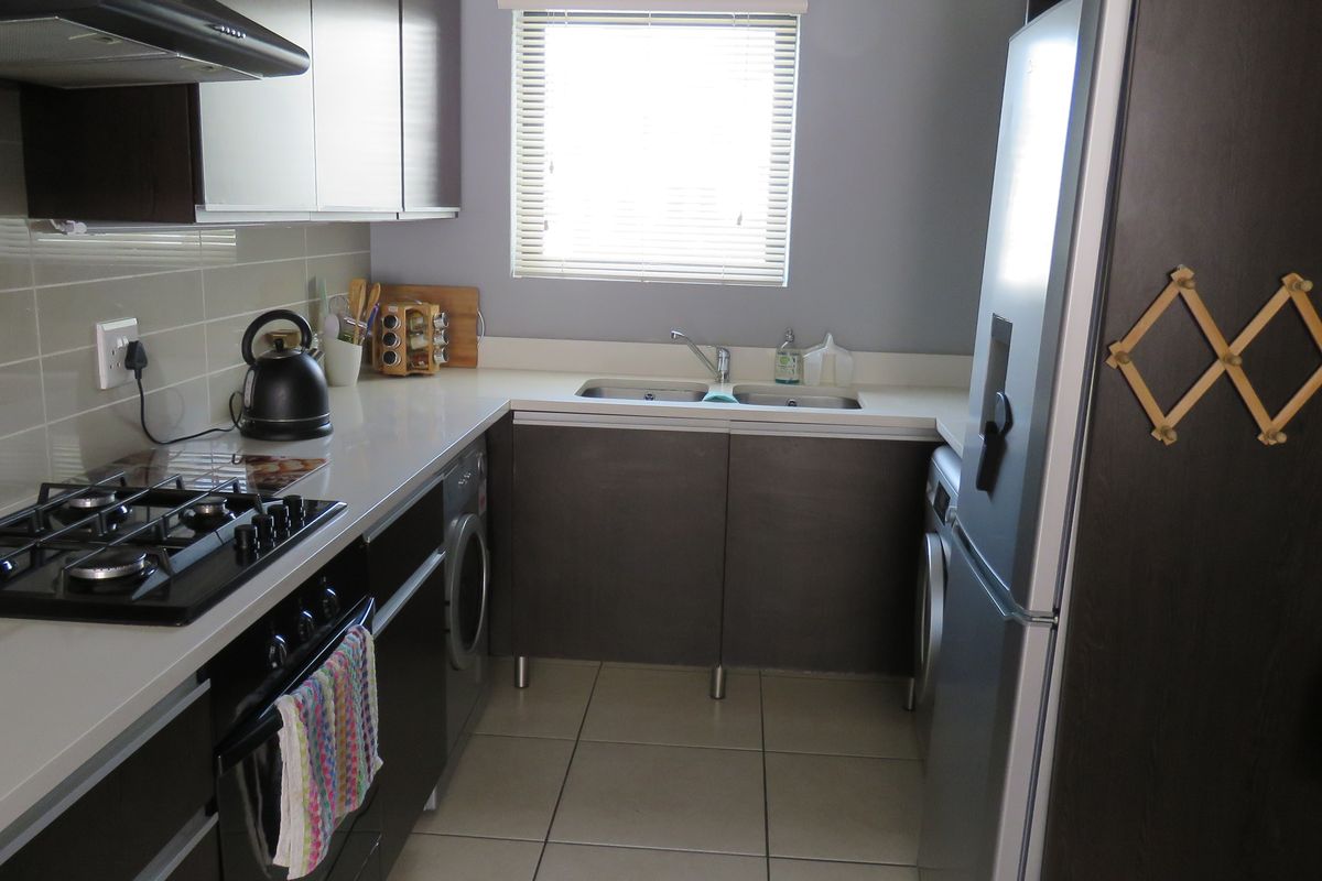 A functional kitchen featuring dark cabinetry, a gas hob, built-in oven, extractor fan, and tiled flooring with a window for natural light.