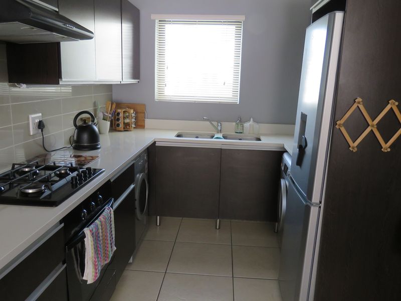 A functional kitchen featuring dark cabinetry, a gas hob, built-in oven, extractor fan, and tiled flooring with a window for natural light.