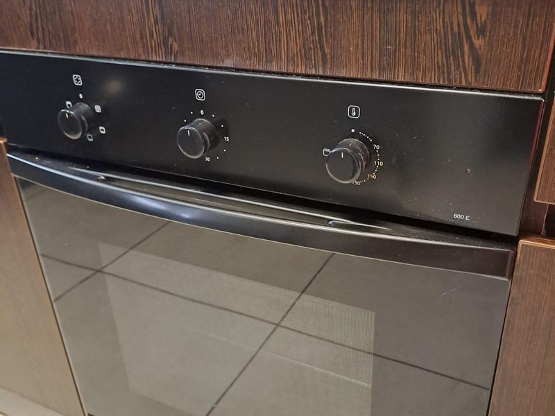 Close-up view of a built-in Defy oven and hob integrated into dark wood-look kitchen cabinetry with tiled flooring.