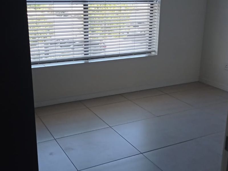 A bright, empty bedroom featuring neutral tiled flooring and fitted venetian blinds, offering a clean and versatile space ready for personalization.