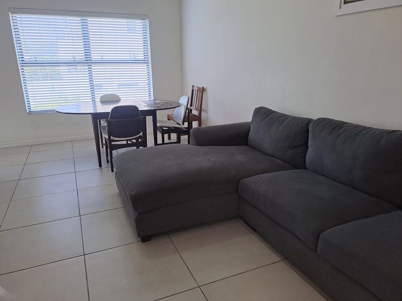 A living area featuring neutral tiled flooring and large windows fitted with venetian blinds, providing a bright and functional space.