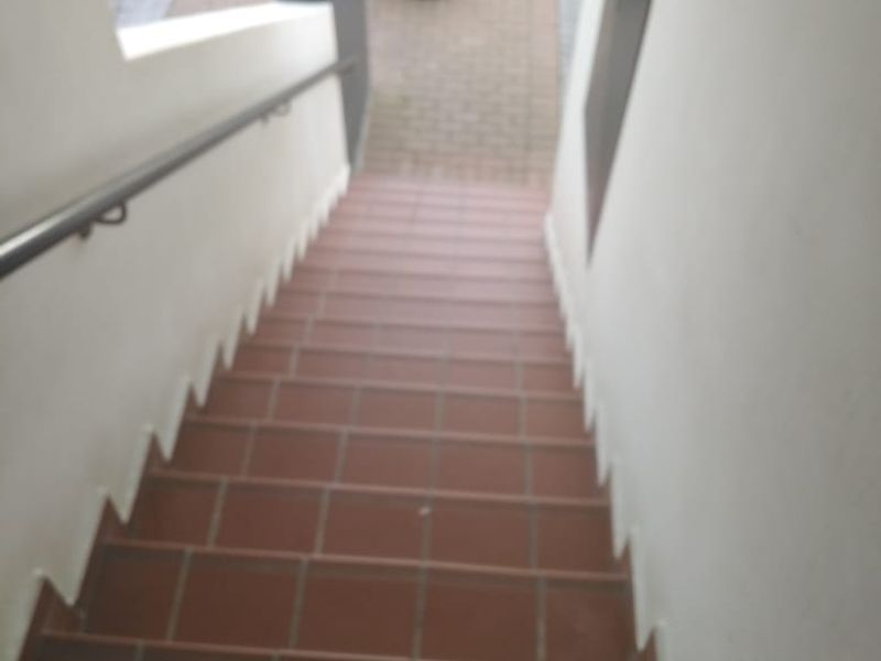 An exterior staircase with tiled steps and a metal handrail leading down to a paved walkway.