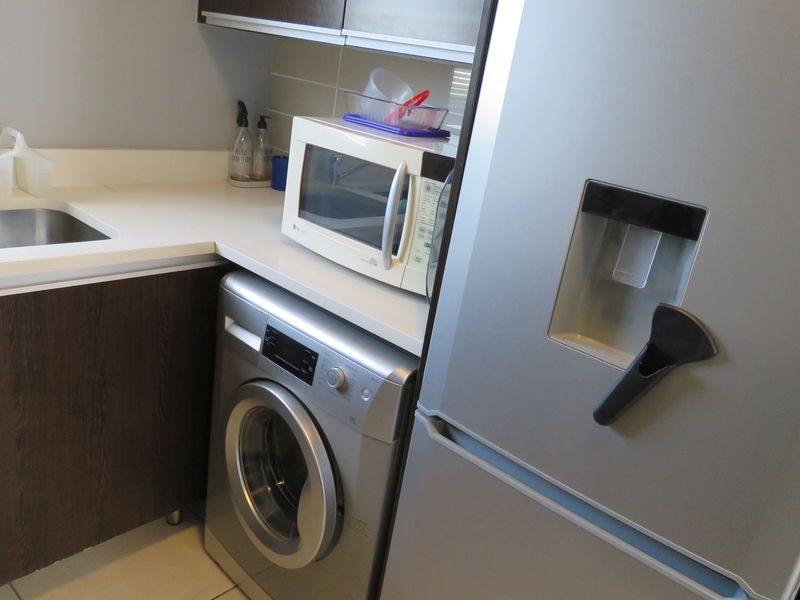 A functional laundry area featuring built-in dark wood cabinetry, a stainless steel sink, and tiled flooring, providing efficient space for utility tasks.