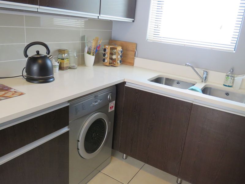 A functional kitchen featuring dark wood cabinetry, white stone countertops, a double stainless steel sink, and a built-in washing machine.