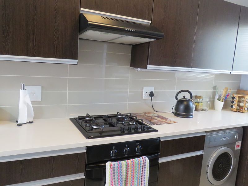 Modern kitchen featuring dark wood cabinetry, a gas hob with extractor fan, built-in oven, and integrated washing machine with a clean tiled backsplash.