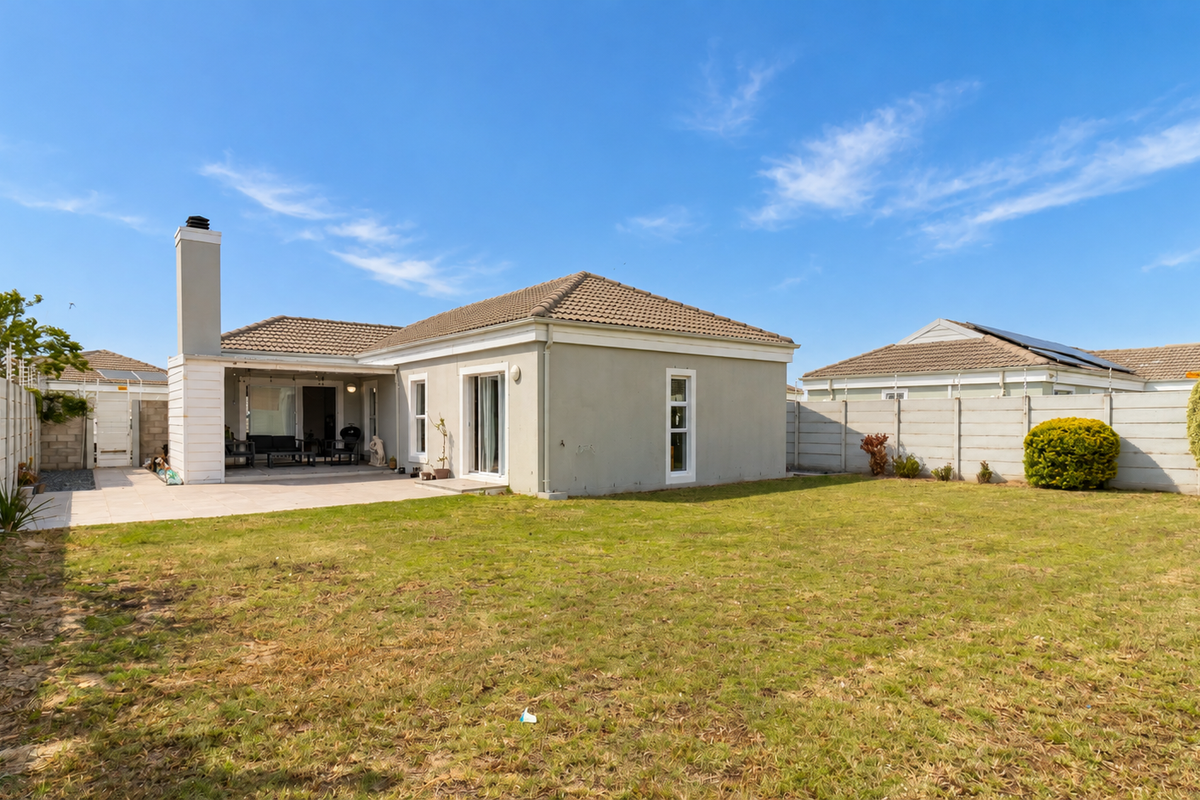 Rear view of the property featuring a paved patio, chimney, sliding glass doors, and a spacious garden enclosed by precast concrete boundary walls.