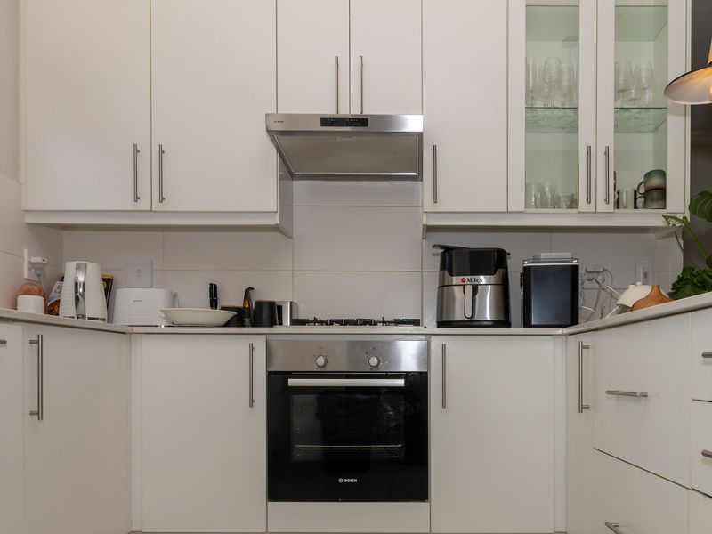 A modern, well-maintained kitchen featuring white cabinetry, stainless steel appliances, a gas hob, and a tiled backsplash.
