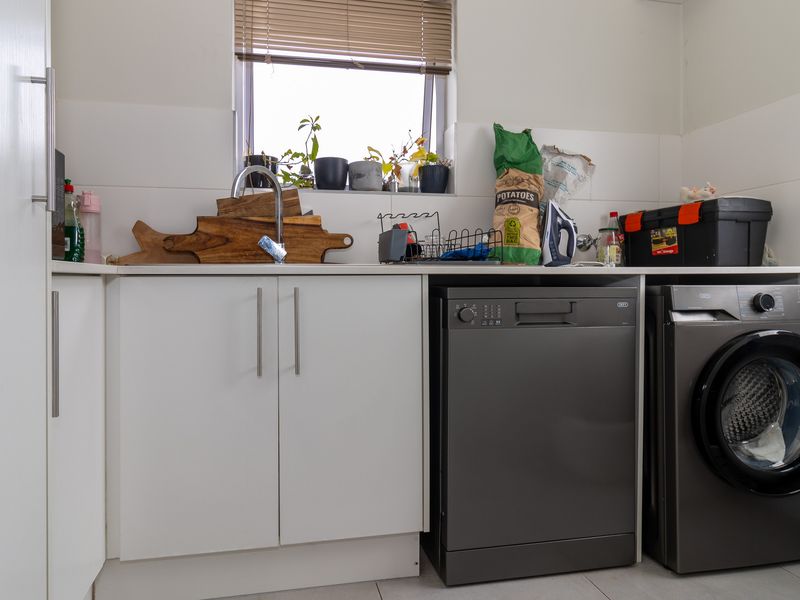 A functional laundry area featuring white built-in cabinetry, a stainless steel sink, and space for integrated appliances.