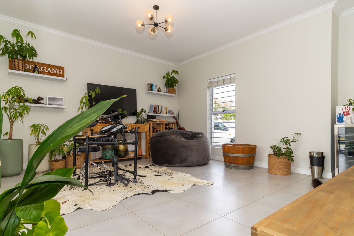A bright and spacious living room featuring neutral tiled flooring, crown molding, and built-in shelving, offering a versatile and well-maintained living space.