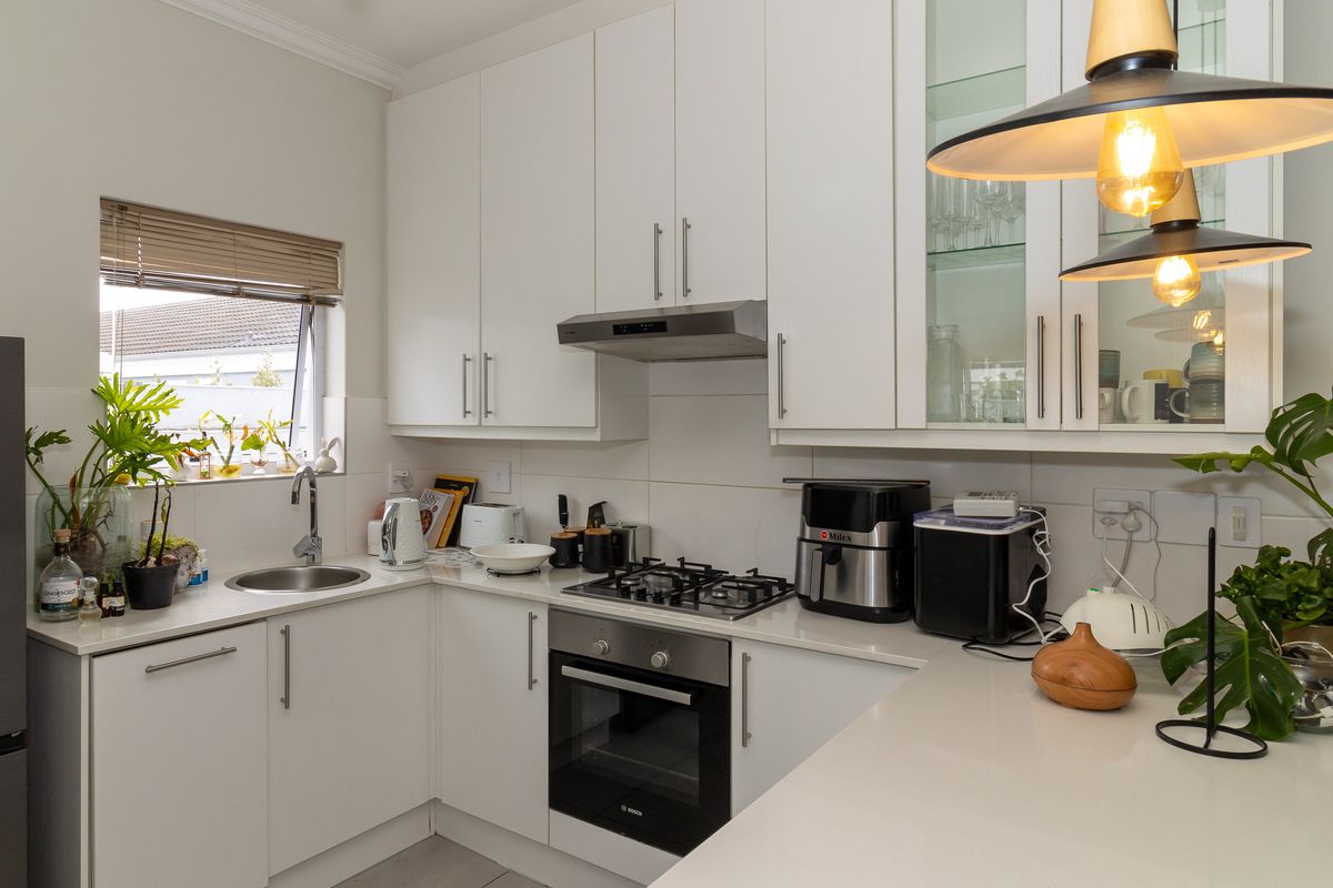 Modern kitchen featuring white cabinetry, stone countertops, integrated gas hob, built-in oven, and a stainless steel sink with a tiled backsplash.