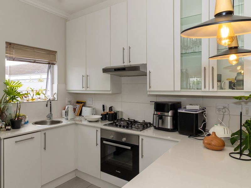 Modern kitchen featuring white cabinetry, stone countertops, integrated gas hob, built-in oven, and a stainless steel sink with a tiled backsplash.