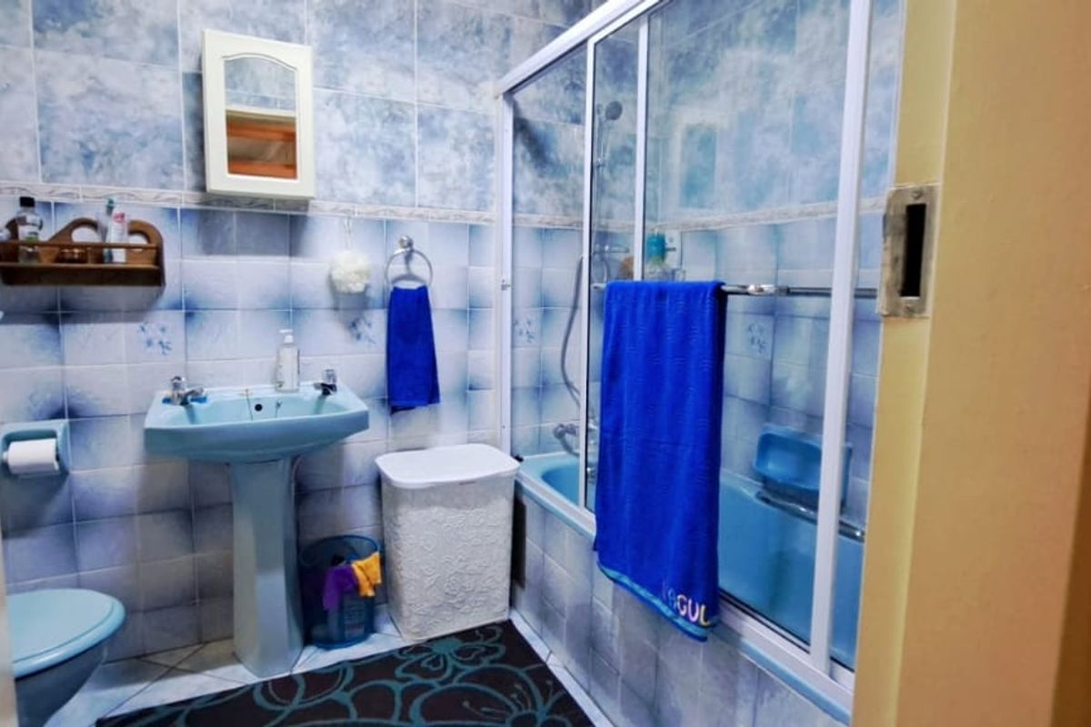A dated bathroom featuring blue sanitaryware, a pedestal basin, and a bathtub with a sliding shower screen, finished with patterned wall tiles.