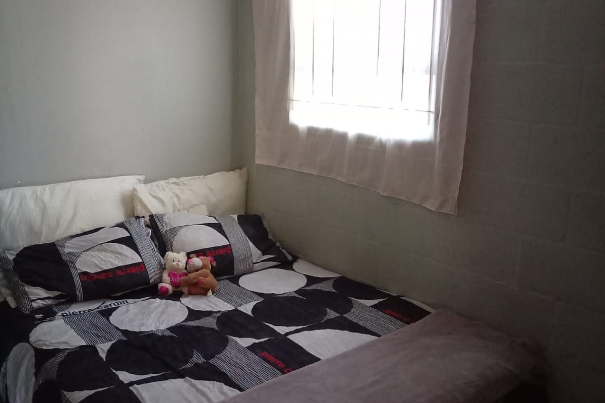 A compact bedroom featuring tiled flooring, a single window with curtain rod, and exposed masonry block wall finish.
