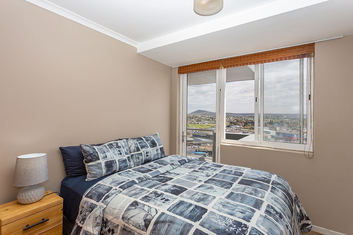 A bedroom featuring a large window with expansive city views, neutral wall tones, and a ceiling-mounted light fixture.