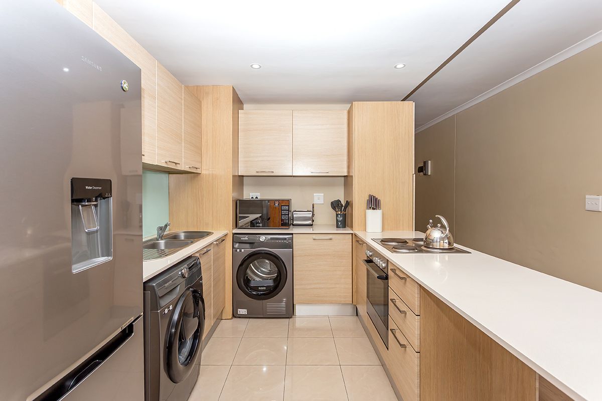 Modern kitchen featuring light wood cabinetry, stone countertops, integrated oven, electric hob, and dedicated space for laundry appliances.
