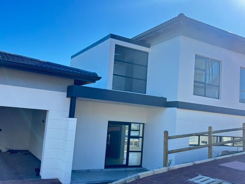 Modern townhouse exterior featuring a clean white facade, dark roof tiles, large aluminium windows, and an integrated garage with a paved driveway.