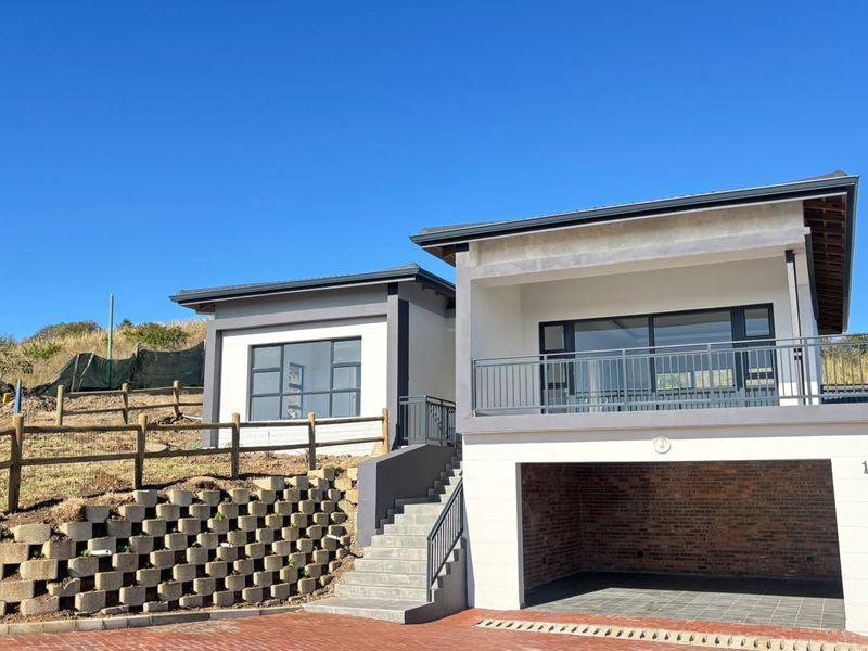 Modern townhouse exterior featuring a double garage, elevated balcony with metal railings, and tiered retaining walls set against a clear blue sky.