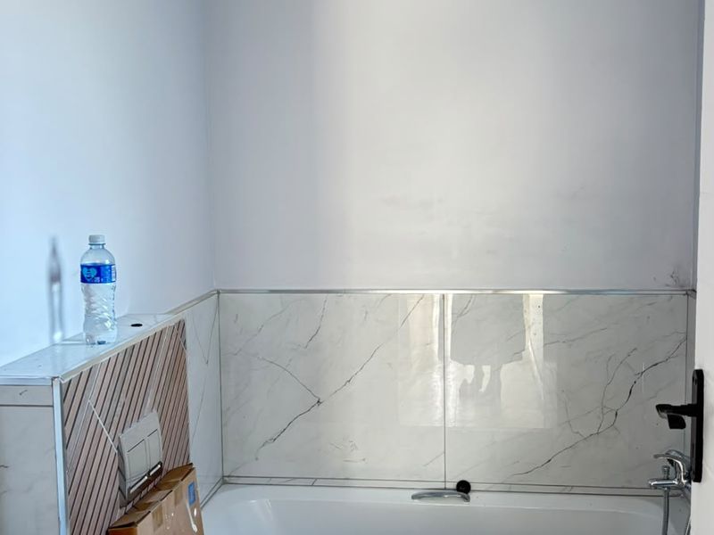 A modern bathroom featuring a built-in bathtub, wall-hung toilet with concealed cistern, and marble-look tiling, currently in the final stages of installation.