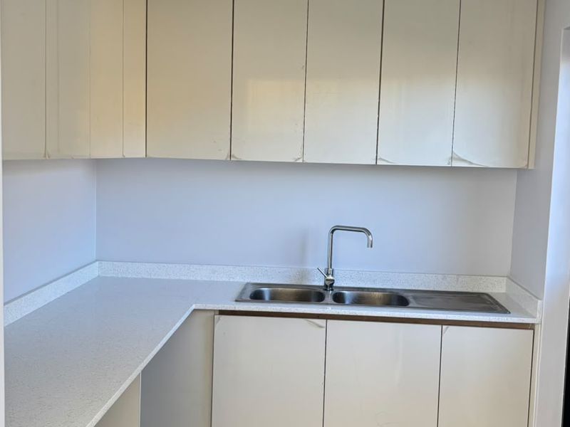 A compact kitchen area featuring built-in cabinetry, stone countertops, and a double bowl sink, currently vacant and awaiting finishing touches.