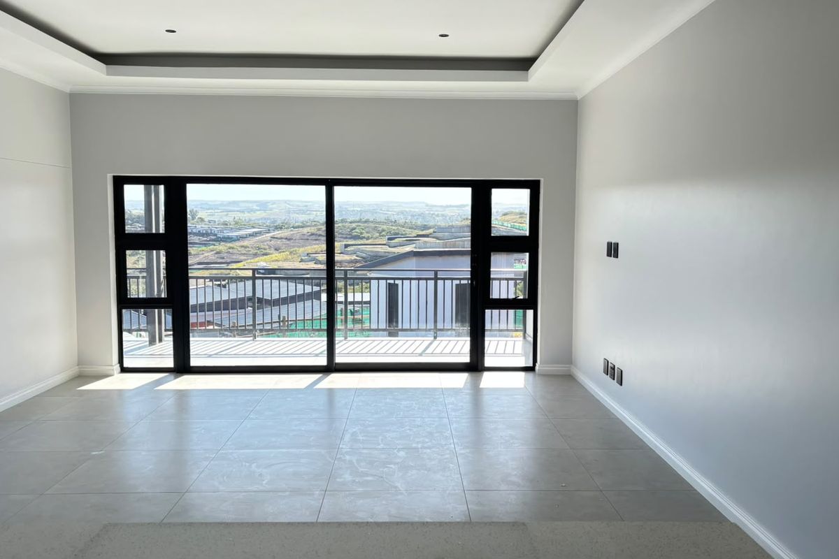 A bright, empty living room featuring modern tiled floors, recessed ceiling lighting, and large sliding glass doors opening to a balcony with scenic views.