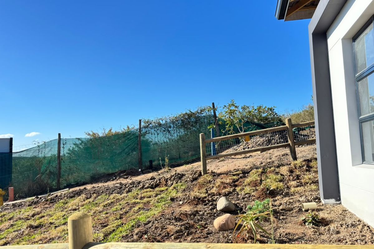 A view of the rear exterior area featuring timber fencing, green shade netting, and an unfinished garden space with exposed soil.