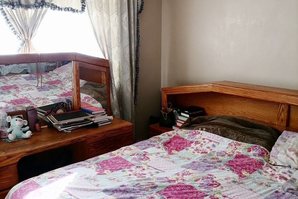 A bedroom featuring neutral wall tones, tiled flooring, and a window dressed with traditional curtains.