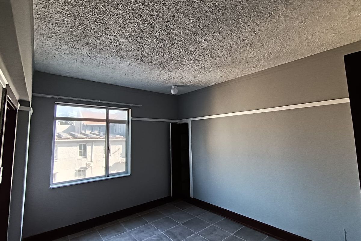 A vacant bedroom featuring tiled flooring, a textured ceiling, and a window providing natural light.
