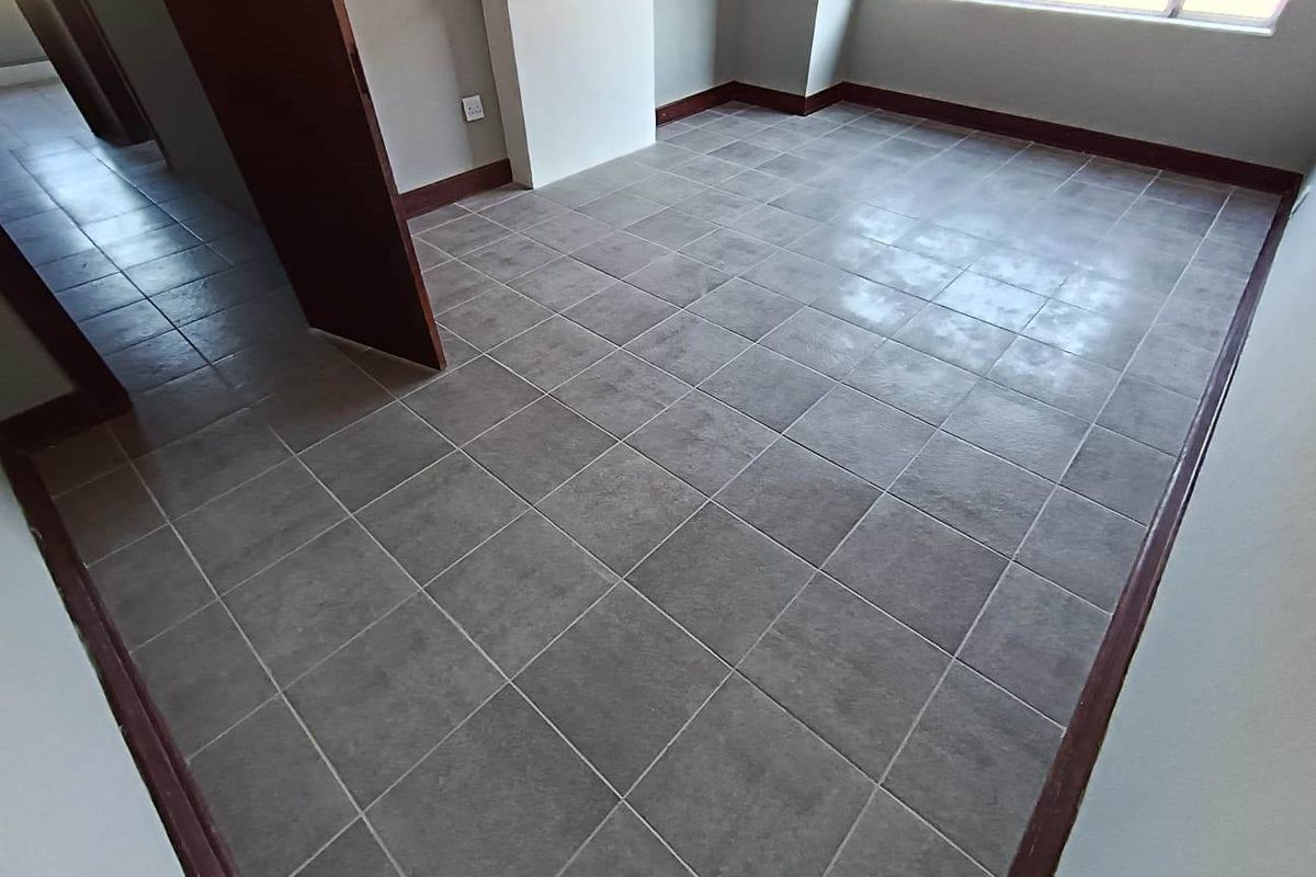 An empty bedroom featuring grey tiled flooring, dark wood skirting boards, and a built-in fireplace mantle.