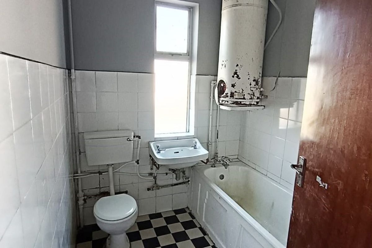 A dated bathroom featuring a bathtub, toilet, wall-mounted basin, and a significantly aged water heater unit.