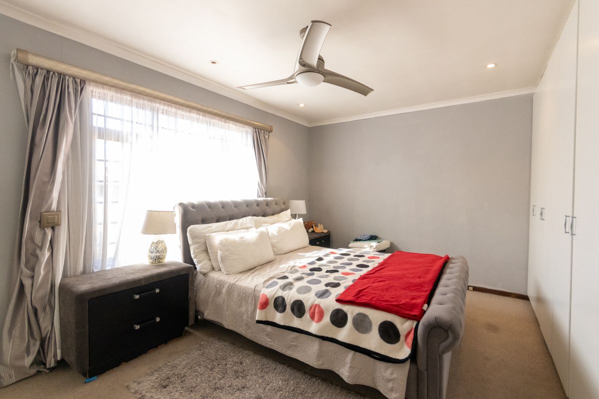 A well-maintained bedroom featuring built-in cupboards, a modern ceiling fan, and large windows allowing for ample natural light.
