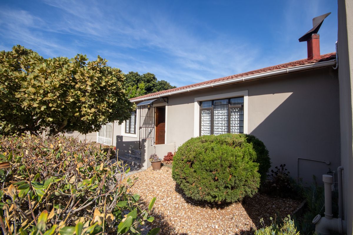 A view of the property's exterior side elevation featuring a tiled roof, security-grilled windows, and a landscaped garden area with gravel beds.