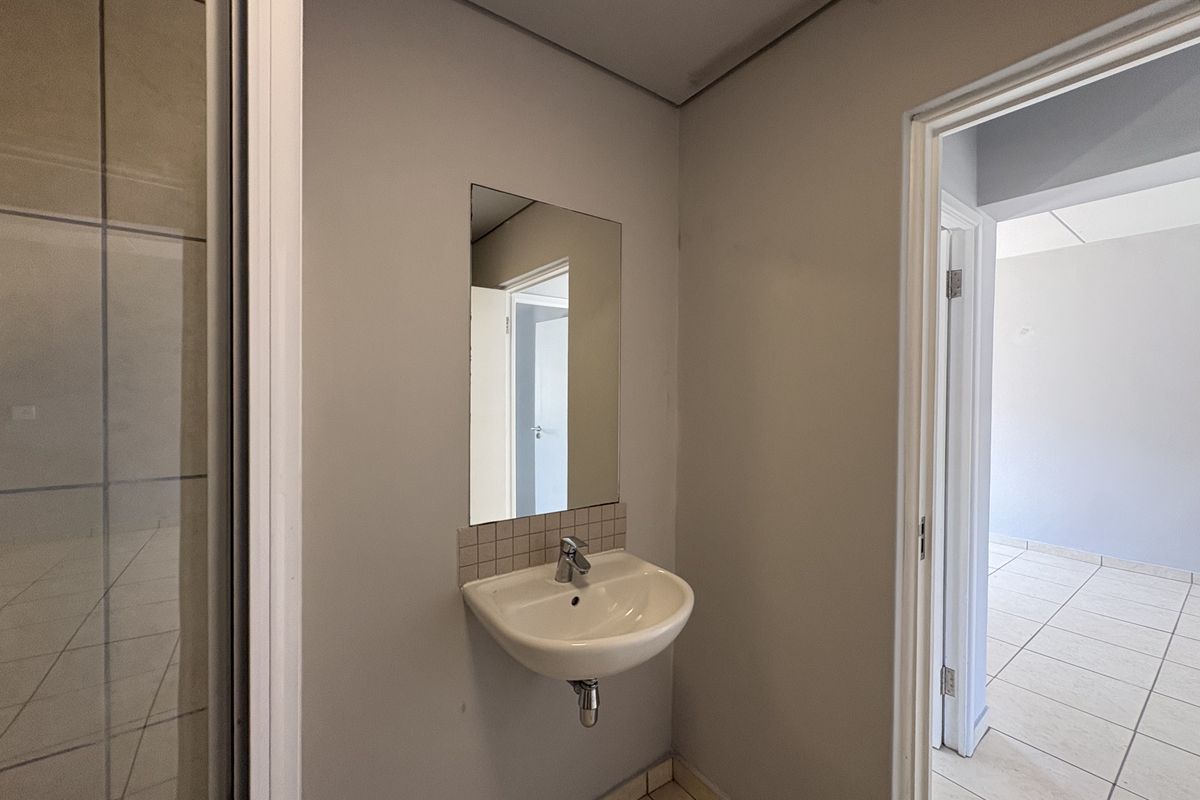 A functional bathroom area featuring a wall-mounted basin, a simple mirror, and tiled flooring, providing a clean and practical space.